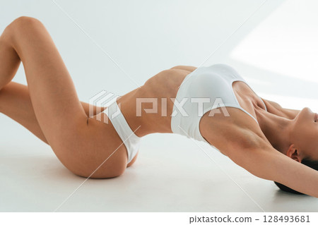 Stretching on the floor, close up view. Young woman with slim body type is in fitness clothes in the studio Stretching on the floor, close up view. Young woman with slim body type is in fitness clothes in the studio 128493681