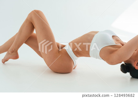 Stretching on the floor, close up view. Young woman with slim body type is in fitness clothes in the studio Stretching on the floor, close up view. Young woman with slim body type is in fitness clothes in the studio 128493682
