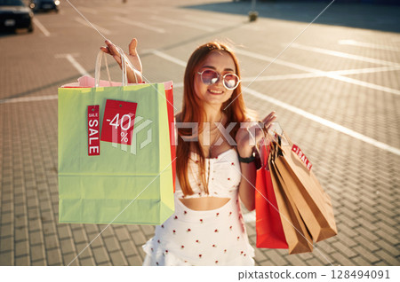 Crazy sales sticker. Beautiful woman in casual clothes is holding shopping bags, outdoors 128494091