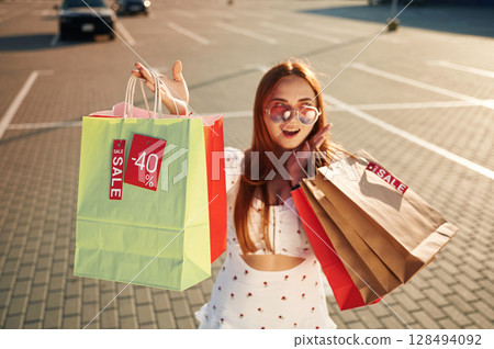 Crazy sales sticker. Beautiful woman in casual clothes is holding shopping bags, outdoors 128494092