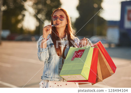 Holding colorful shopping bags. Beautiful woman in casual clothes, outdoors 128494104