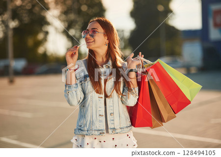 Holding colorful shopping bags. Beautiful woman in casual clothes, outdoors 128494105