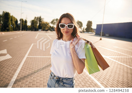 In sunglasses. Beautiful woman in casual clothes is holding shopping bags, outdoors 128494238