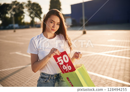 Minus fifty percent sale. Half the price. Beautiful woman in casual clothes is holding shopping bags, outdoors Minus fifty percent sale. Half the price. Beautiful woman in casual clothes is holding shopping bags, outdoors 128494255