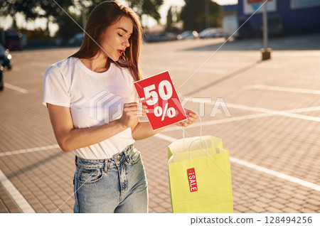 Minus fifty percent sale. Half the price. Beautiful woman in casual clothes is holding shopping bags, outdoors 128494256