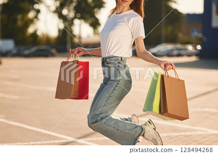 Close up view. Beautiful woman in casual clothes is holding shopping bags, outdoors 128494268