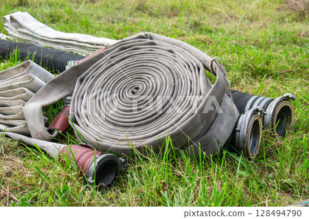 Fire hose rolled up on lawn, lying on grass Fire hose rolled up on lawn, lying on grass 128494790
