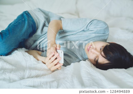 Young man watching smartphone in bed Young man watching smartphone in bed 128494889
