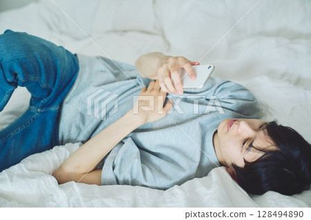 Young man watching smartphone in bed Young man watching smartphone in bed 128494890