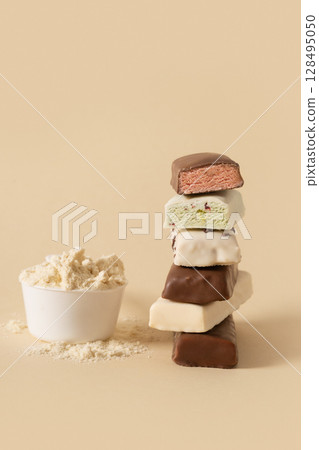 Different whey protein bars with various coatings and sprinkles scoop of protein powder on beige background. Fitness nutrition. Vertical format. Different whey protein bars with various coatings and sprinkles scoop of protein powder on beige background. Fitness nutrition. Vertical format. 128495050