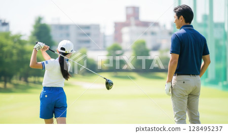 A girl practices her driver shot while being watched by her coach A girl practices her driver shot while being watched by her coach 128495237