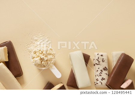 Different whey protein bars with various coatings and sprinkles scoop of protein powder on beige background. Healthy fitness nutrition. View from above. Copy space 128495441