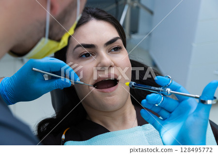 A dentist examines a patient's mouth using specialized tools during a dental procedure in a bright and modern dental office environment, ensuring proper oral health care. 128495772