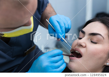 A Dentist Using Dental Instruments to Examine a Patient's Teeth for Health and Wellness in a Modern Clinic Environment 128495824