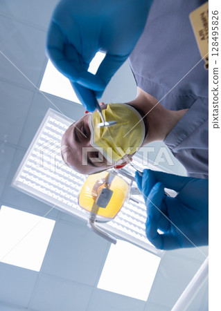 Professional Dentist Performing Dental Procedure with Precision and Care in a Modern Office, Taking Every Precaution with Protective Gear for Patient Safety and Comfort 128495826