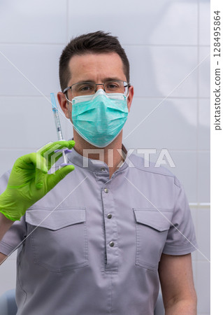 A Healthcare Professional in Protective Gear Holding a Syringe Ready for Vaccination or Injection Procedure with a Focused Expression in a Clinical Setting 128495864