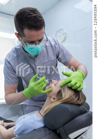 A Professional Aesthetic Treatment in Progress: Expert Injector Administering Botox or Fillers in a Modern Clinic Environment to Enhance Patient's Facial Features 128495894