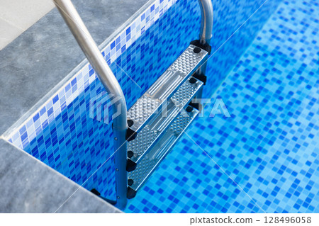 Close-up view of a blue-tiled swimming pool featuring a stainless steel ladder Close-up view of a blue-tiled swimming pool featuring a stainless steel ladder 128496058