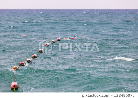 Red plastic buoys float on a line dividing the calm sea surface 128496073