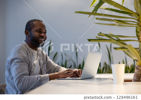 Smiling businessman reacting emotionally while using computer at work desk in professional workspace 128496161