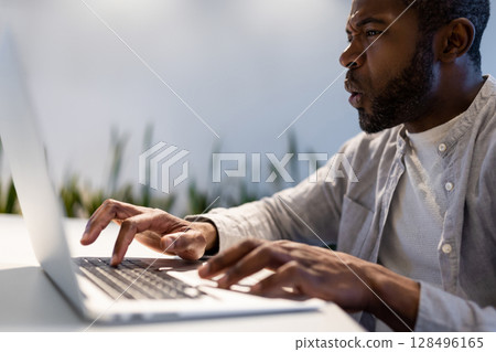 Astonished male employee typing quickly on laptop and looking at screen with surprised expression Astonished male employee typing quickly on laptop and looking at screen with surprised expression 128496165