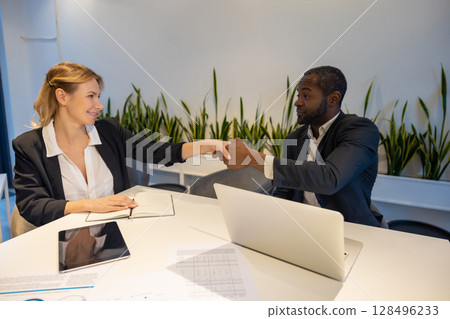 Two colleagues sitting at desk smiling while planning project using laptop tablet and notebook Two colleagues sitting at desk smiling while planning project using laptop tablet and notebook 128496233