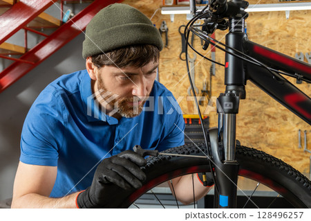 Skilled man repairing bicycle with tools in modern workshop 128496257