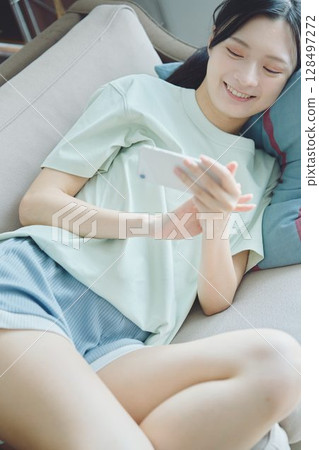 A woman using a smartphone while lying on a sofa A woman using a smartphone while lying on a sofa 128497272