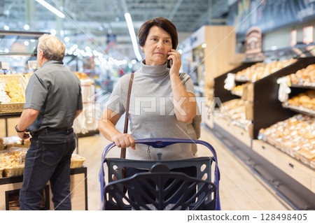 Elderly woman consulting on mobile phone while shopping at grocery store 128498405