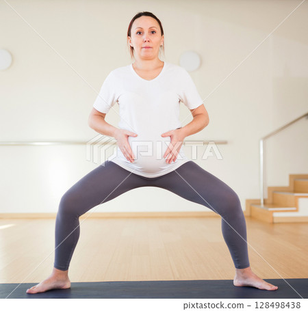 Pregnant woman is engaged in yoga. A pregnant woman practices yoga in the hall. Goddess Pose or utkata konasana 128498438