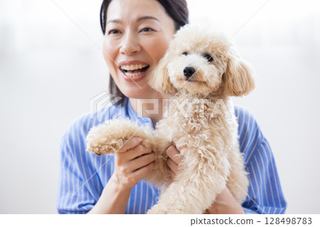 A middle-aged woman holding a Bichon Poo A middle-aged woman holding a Bichon Poo 128498783