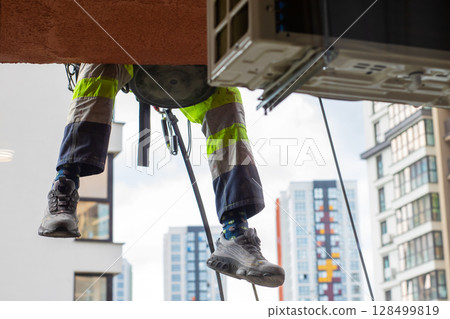 A man is climbing a sturdy ladder to safely install an AC unit 128499819