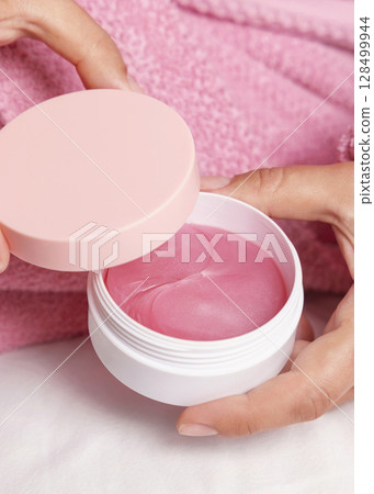 Woman in pink bathrobe holding eye patches jar with pink lid closeup, cosmetic mockup Woman in pink bathrobe holding eye patches jar with pink lid closeup, cosmetic mockup 128499944