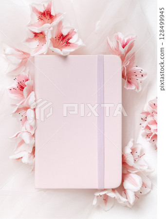 Blank vertical paper card near pink azalea flowers and ribbons top view, spring wedding mockup 128499945