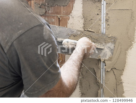 Craftsman uses a float trowel and cement to plaster a house wall. Construction process 128499946