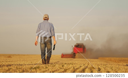 farmer working in wheat field, combine harvester ploughing in wheat field, agriculture tablet, seamless farm management, enhancing farm profitability, integration of technology in crop management 128500235