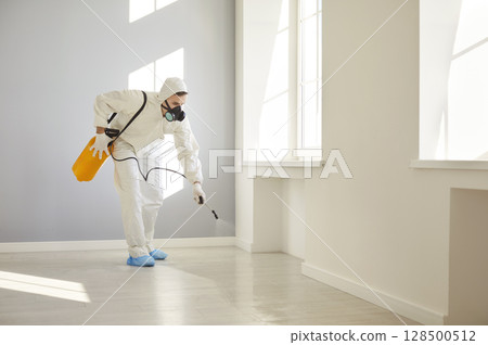 Service man in protective ppe suit disinfecting empty apartment with disinfectant spray 128500512