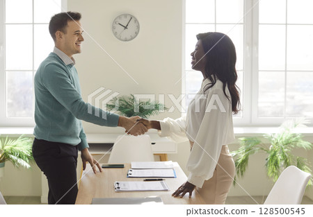 Business people in office making deal. Man and woman shaking hands celebrating business achievement Business people in office making deal. Man and woman shaking hands celebrating business achievement 128500545