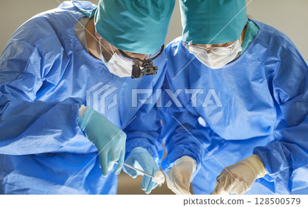 Two skilled professional surgeons performing an operation in modern operating room at hospital. 128500579