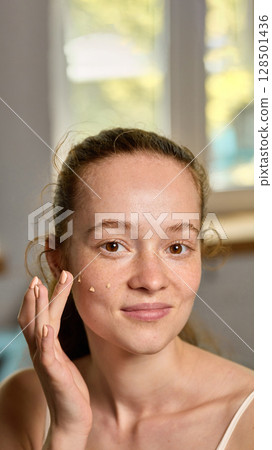 Close-up of woman blending foundation with closed eyes and content smile Close-up of woman blending foundation with closed eyes and content smile 128501436