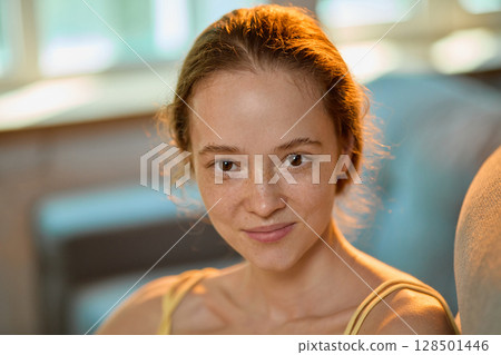 Warm-toned portrait of smiling woman with freckles in relaxed home environment 128501446