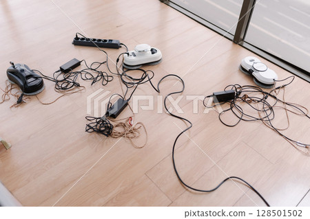 Several window cleaning robots lying on floor, connected to chargers and power strip, prepared for upcoming cleaning tasks at home, no people, nobody. Concept of cleaning house with smart devices. 128501502