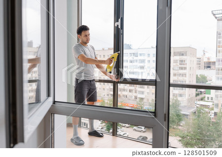 Remote view of professional cleaner male using cordless vacuum cleaner to wash large window in modern office building, ensuring spotless and streak-free shine with specialized equipment. 128501509