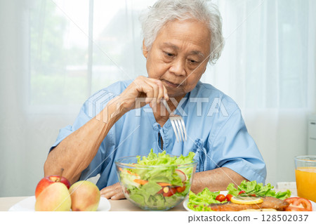 Asian elderly woman patient eating salmon steak breakfast with vegetable healthy food in hospital. 128502037
