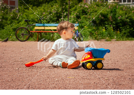 Toddler playing with a toy dump truck on a sunny playground day Toddler playing with a toy dump truck on a sunny playground day 128502101