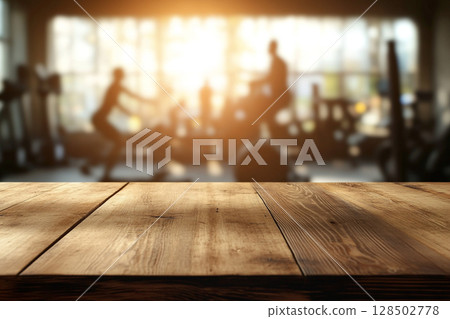 A close-up of a wooden table surface in the foreground, with a blurred gym interior and sunlit windows in the background. 128502778