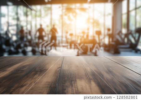 A close-up of a wooden table surface in the foreground, with a blurred gym interior and sunlit windows in the background. 128502801