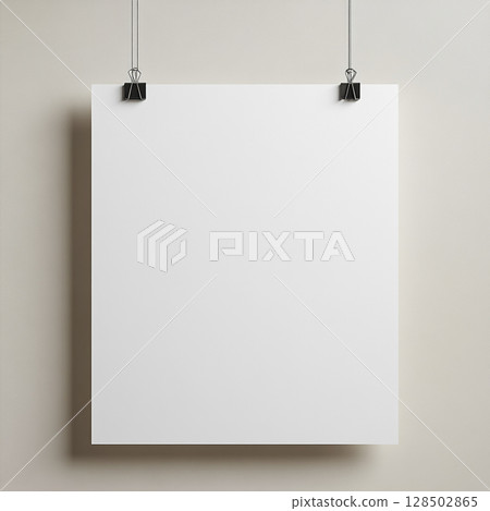 A blank white poster hangs on a grey wall, held by black binder clips. 128502865