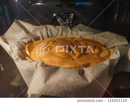 Apple pie baking in the oven on baking paper 128503139
