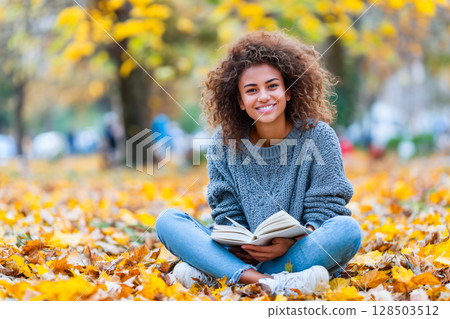 Smiling teenage girl with books in autumn park 128503512